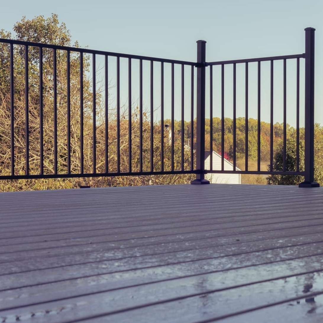 Wooden deck with black metal railing overlooking trees and a distant landscape