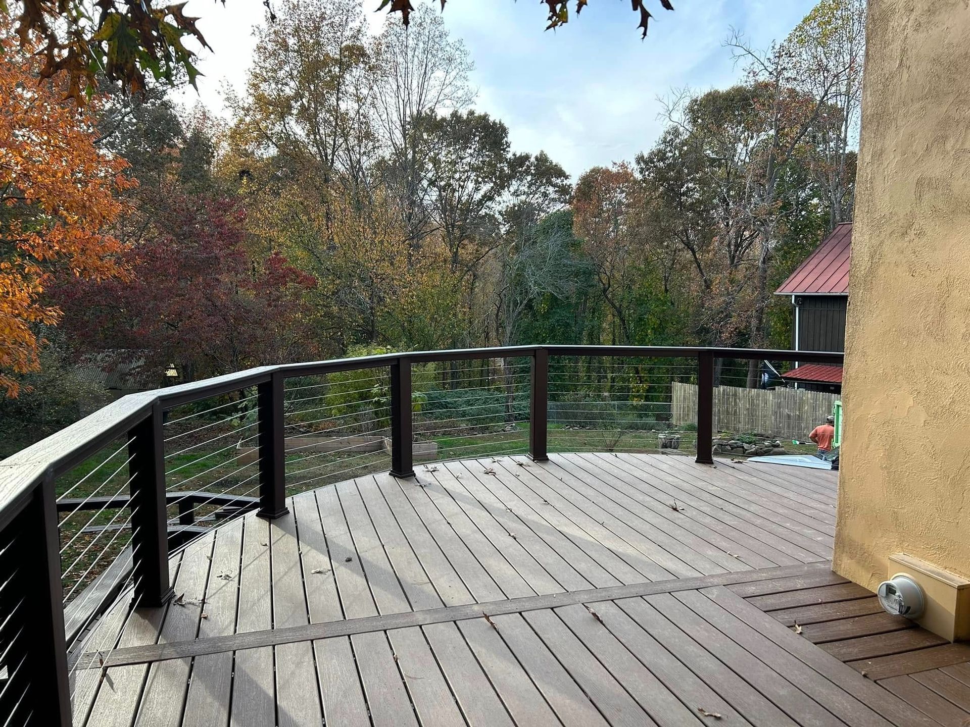 Curved wooden deck with black railing overlooking trees and a house corner