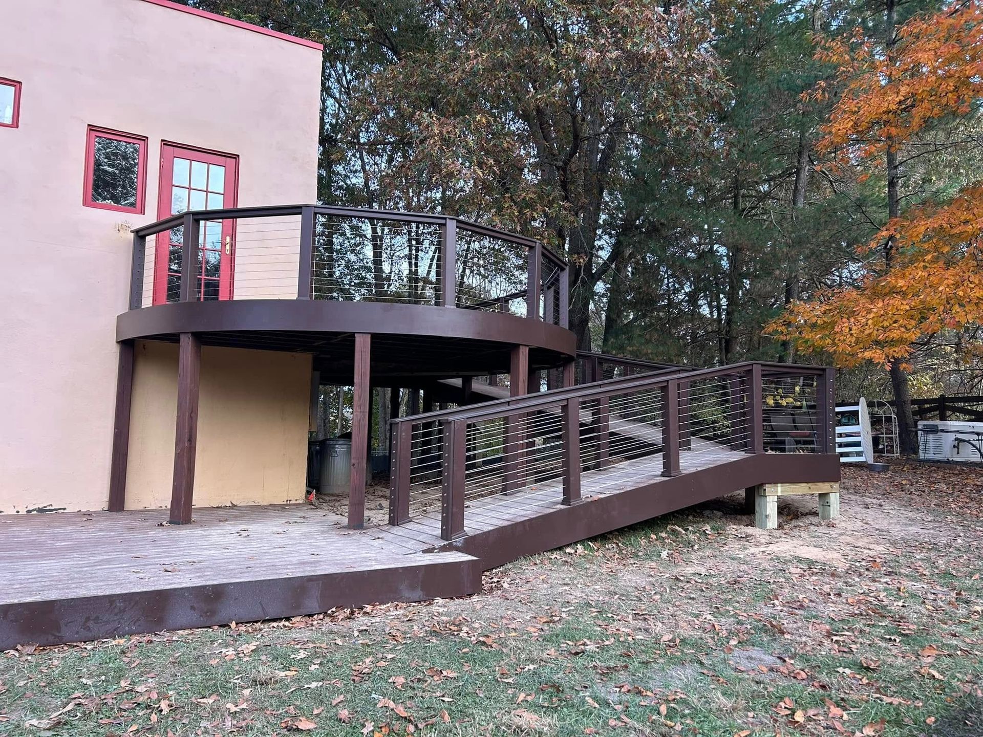 Accessible wooden ramp and raised deck beside a pink house in a wooded yard