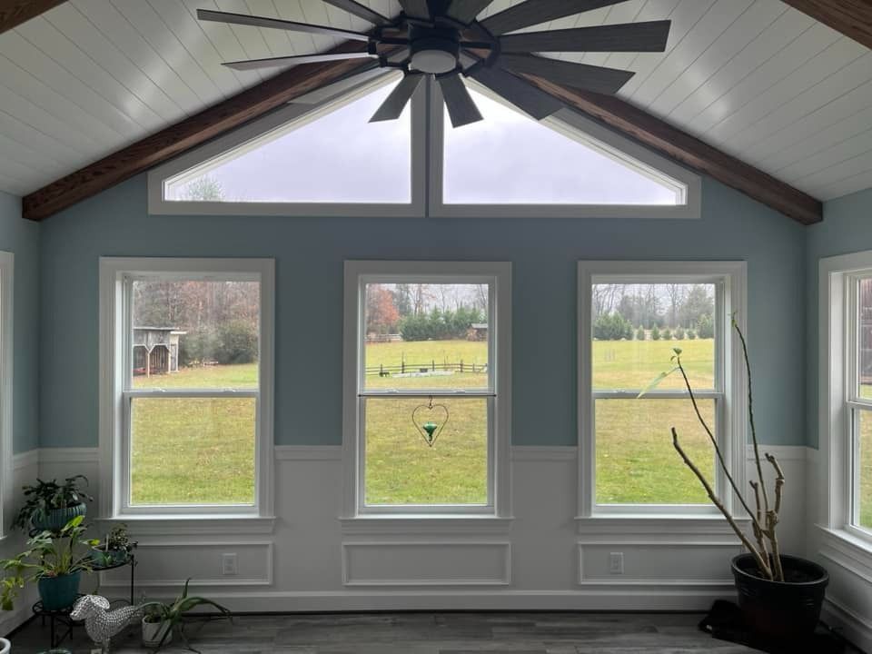 Bright sunroom with three windows, vaulted ceiling, and large ceiling fan overlooking a grassy yard.