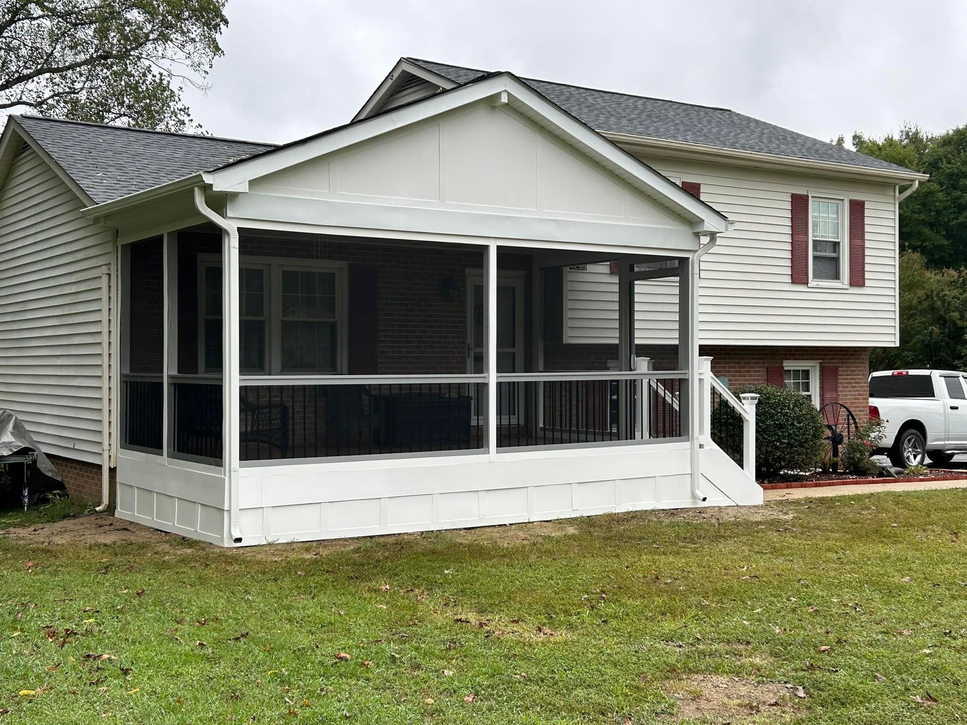 White house with screened front porch and red shutters on a grassy yard