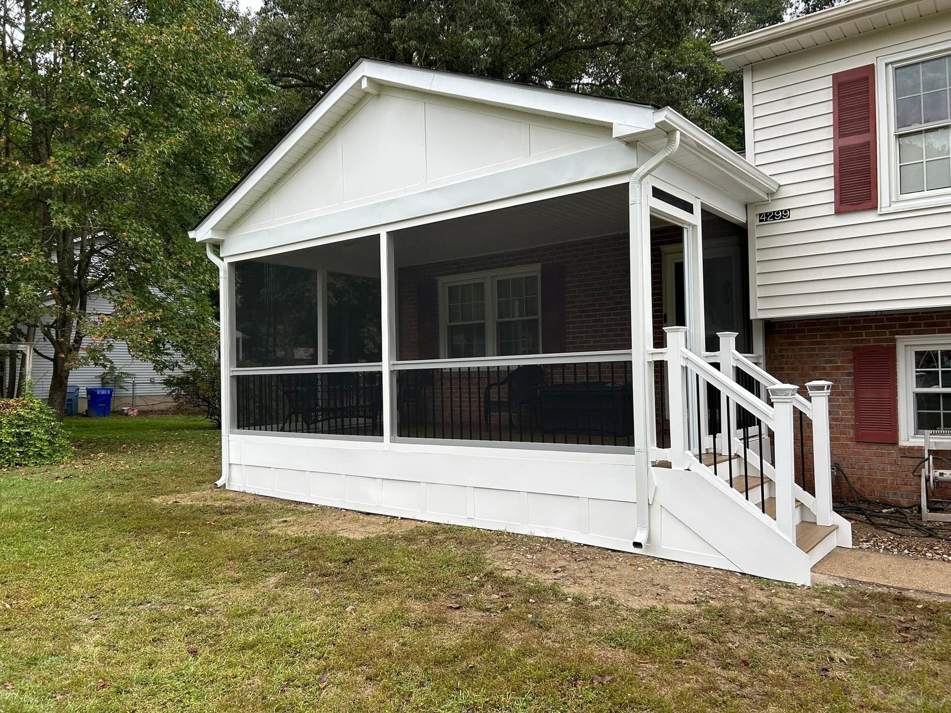 Screened porch with white trim and stairs attached to a house, beside a grassy yard