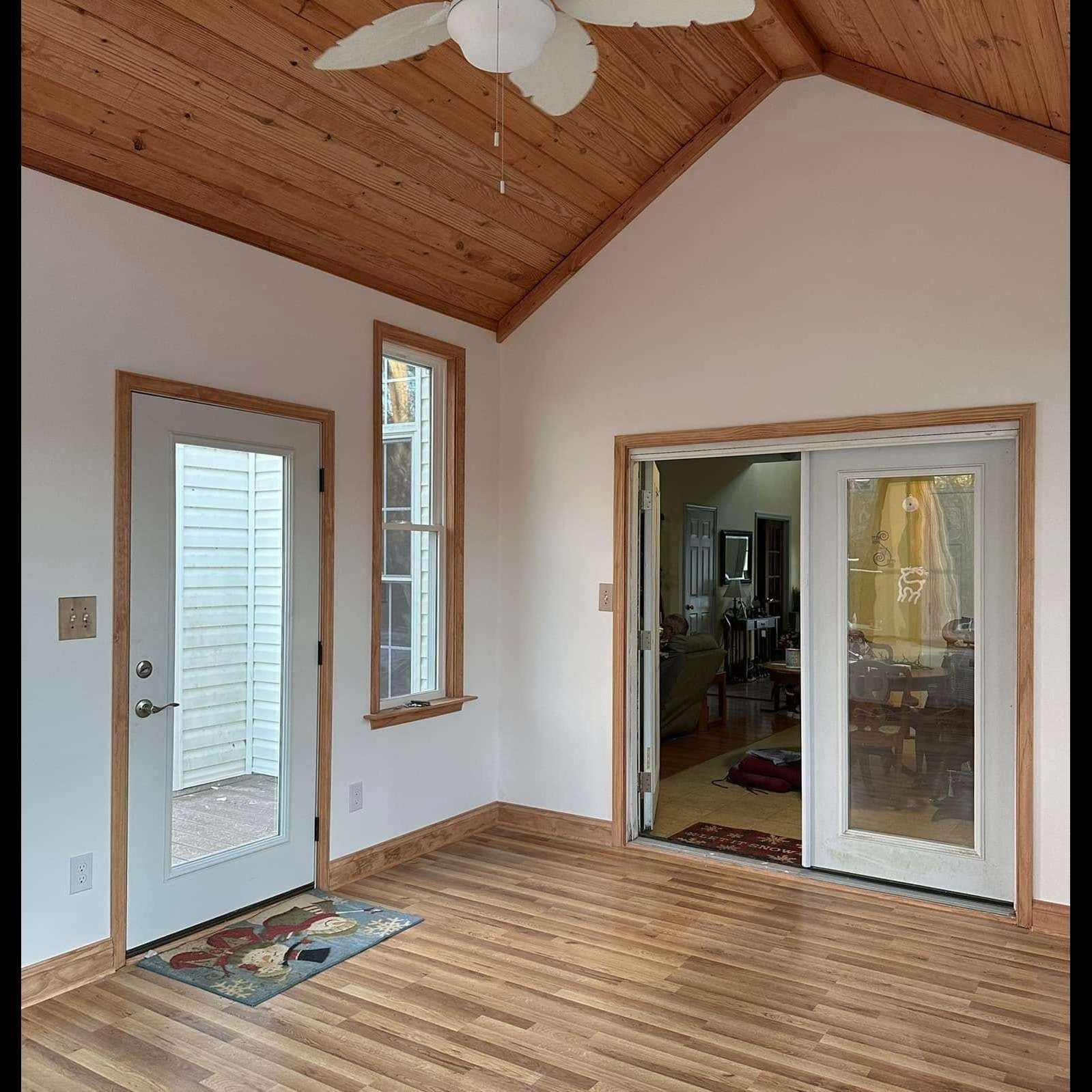 Empty sunroom with wood ceiling, light walls, narrow window, glass door, and sliding doors to an adjacent room