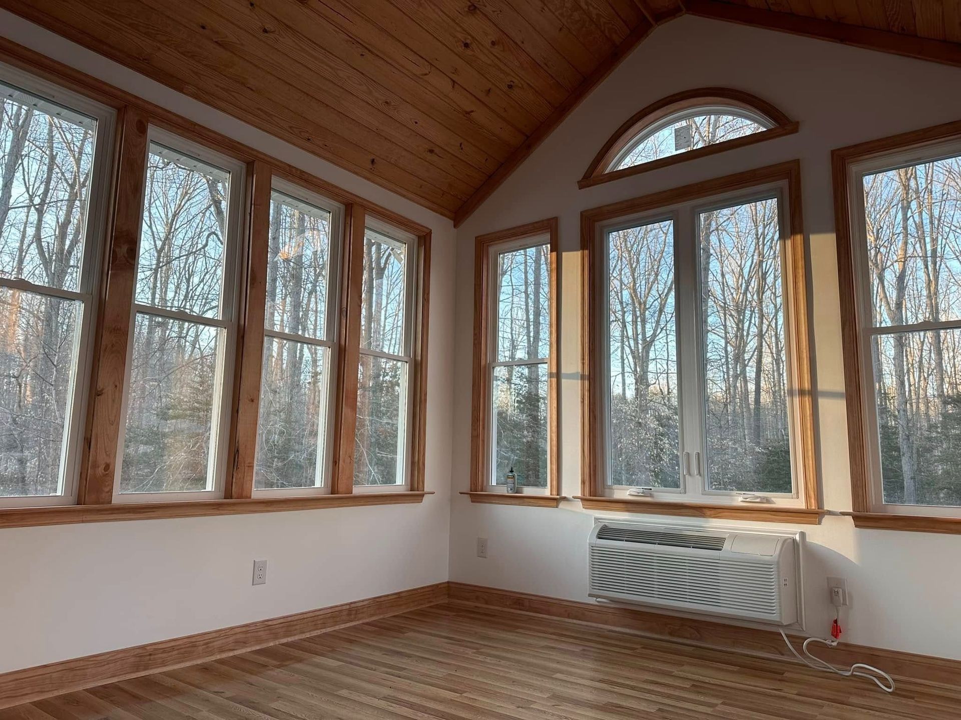 Empty sunroom with large windows, wood ceiling, and a white radiator on the right.