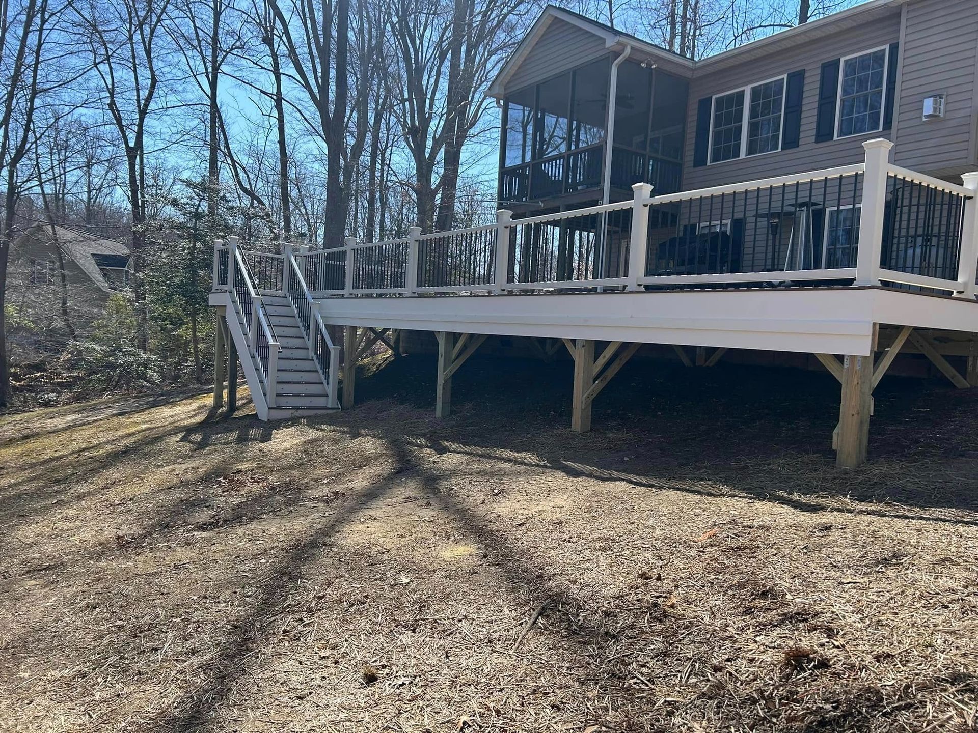 Raised wooden deck beside a house in a wooded yard, with stairs and winter sunlight shadows