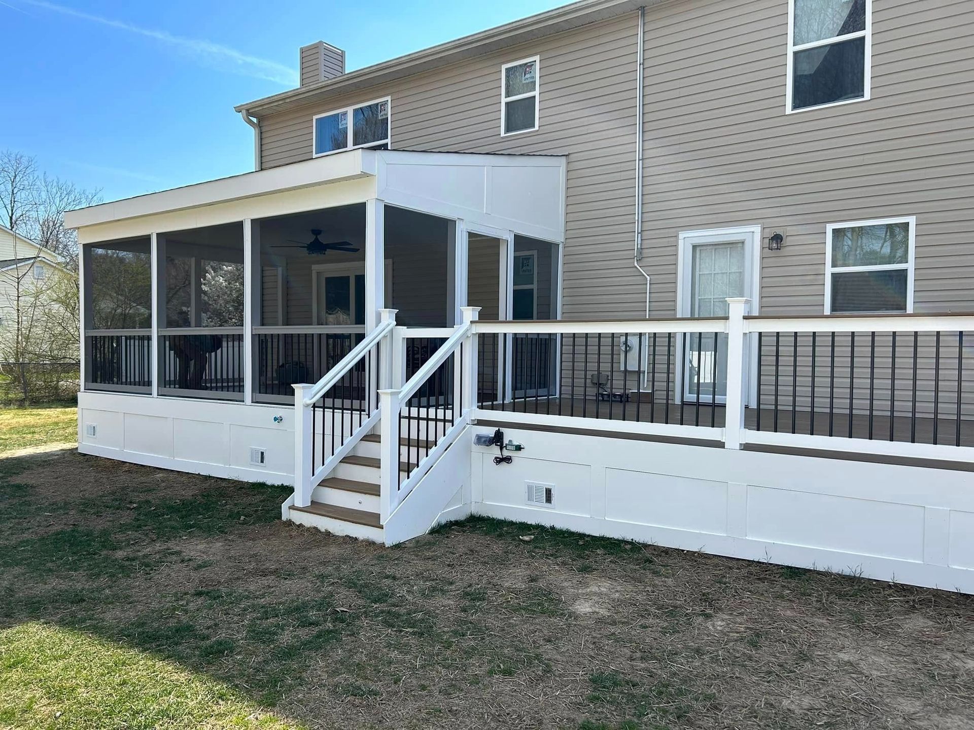 Enclosed white porch with black railing and stairs attached to a tan brick house