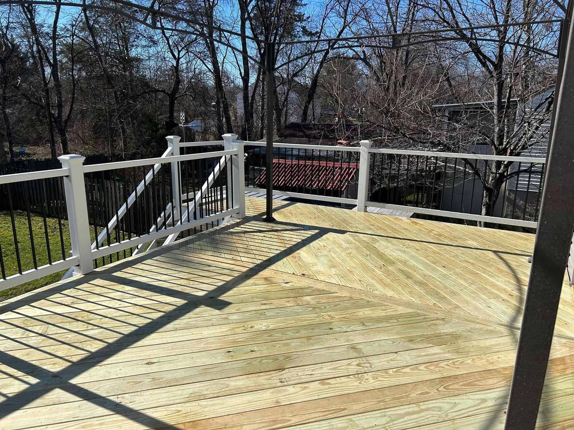 Wooden deck with white railing overlooking leafless trees and a red fence in sunlight