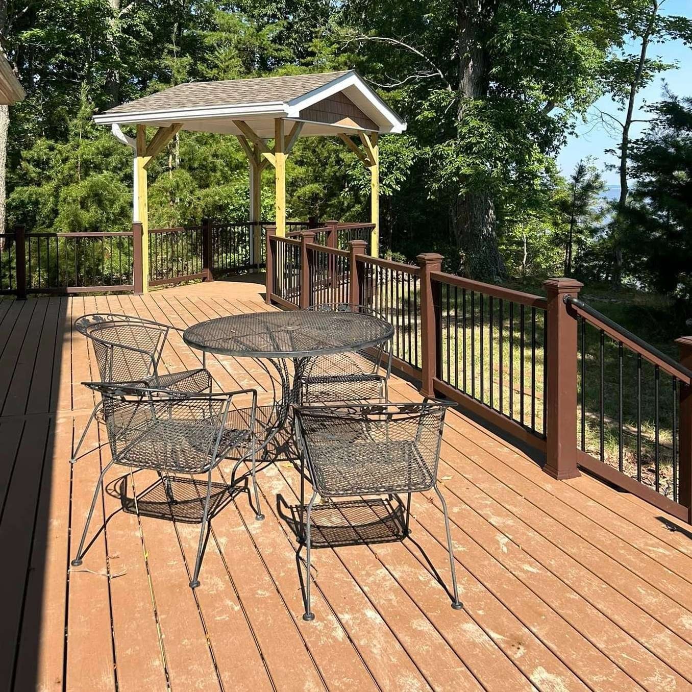 Wooden deck with wire patio table, chairs, and a small covered gazebo overlooking trees and water