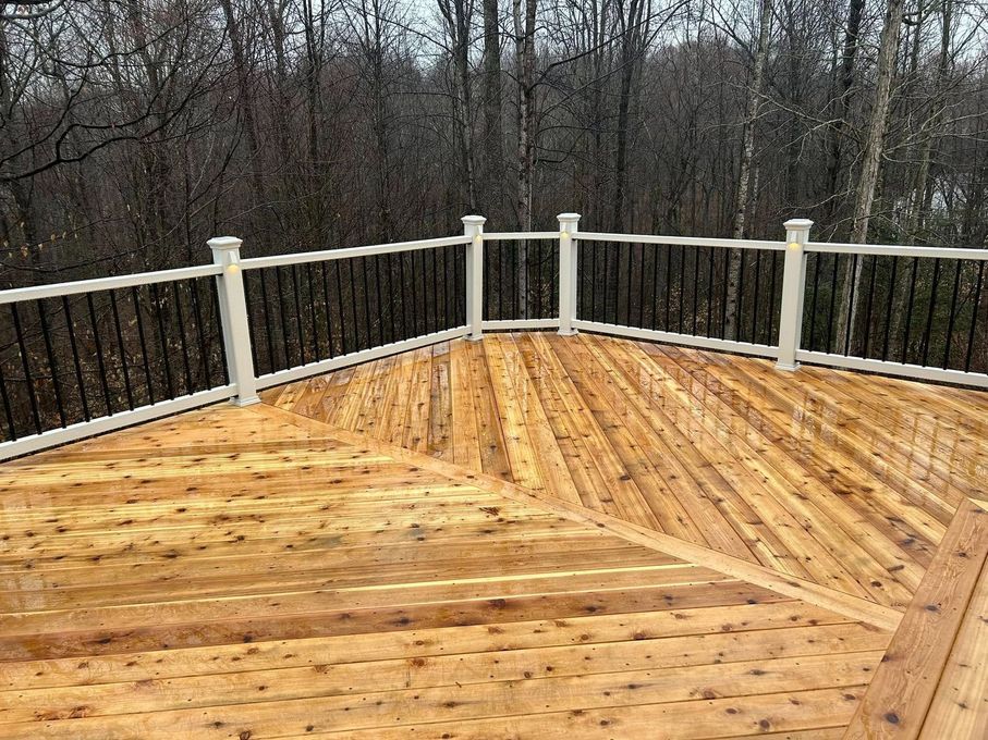 Wooden deck with white railing overlooking bare trees in a wooded area