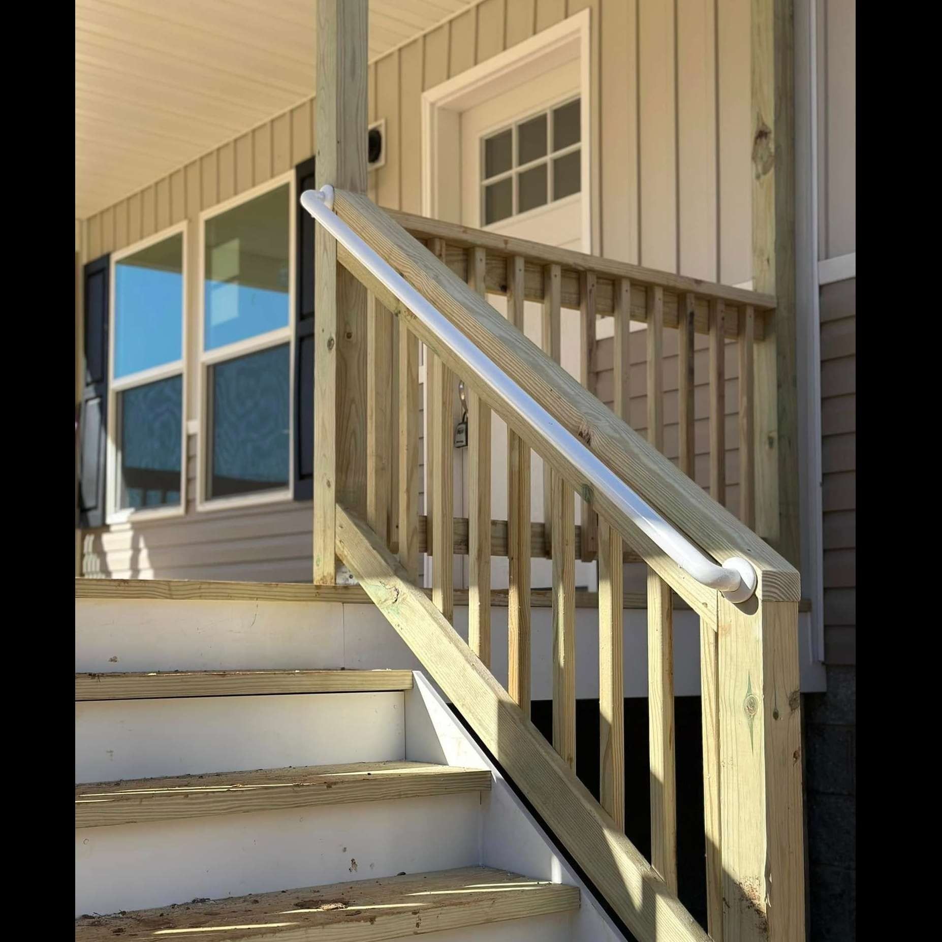 Wooden porch stairs with white railing beside house siding and windows
