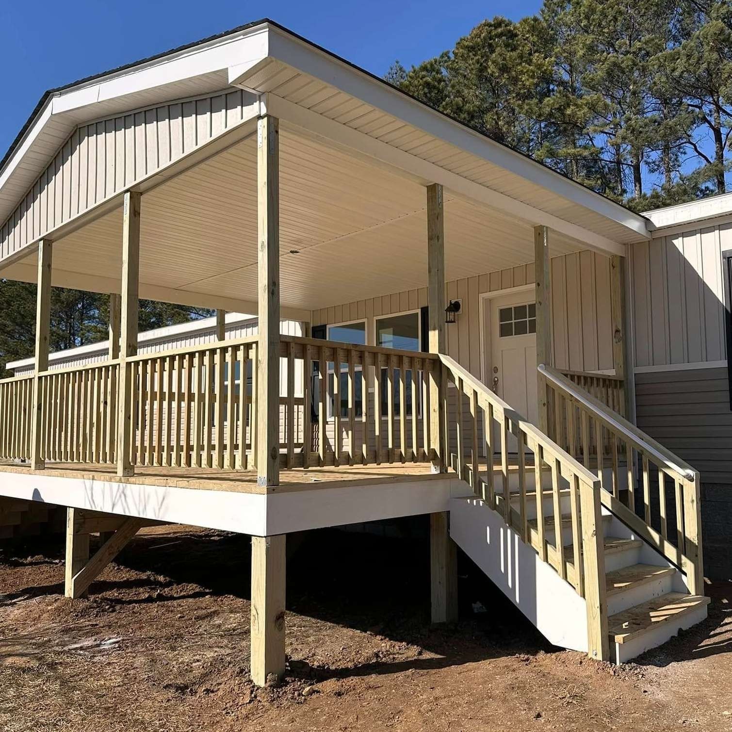 Raised beige house with a front porch, stairs, and white trim in a wooded yard