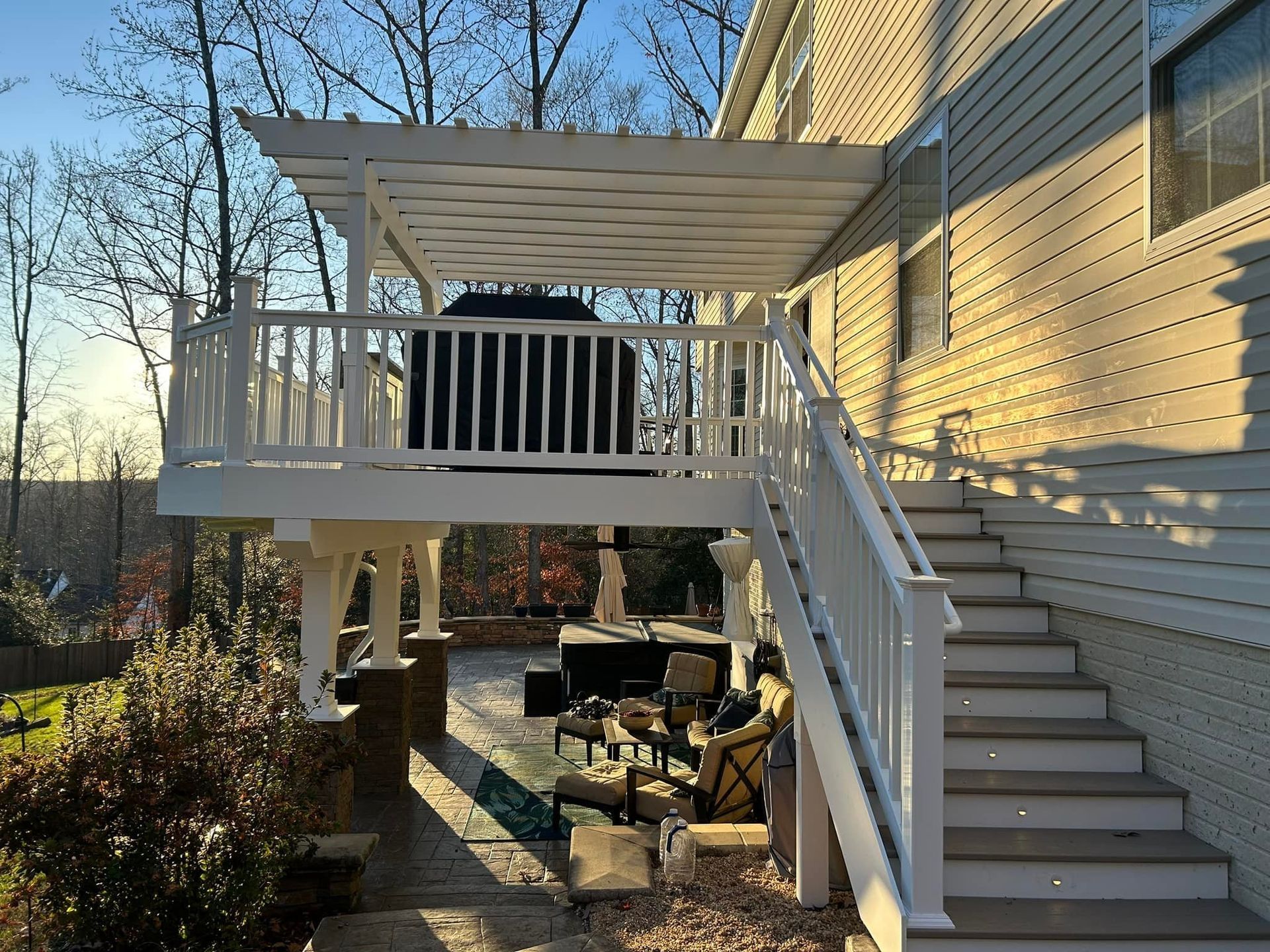 White house deck with stairs, pergola roof, and patio furniture in a sunny backyard.