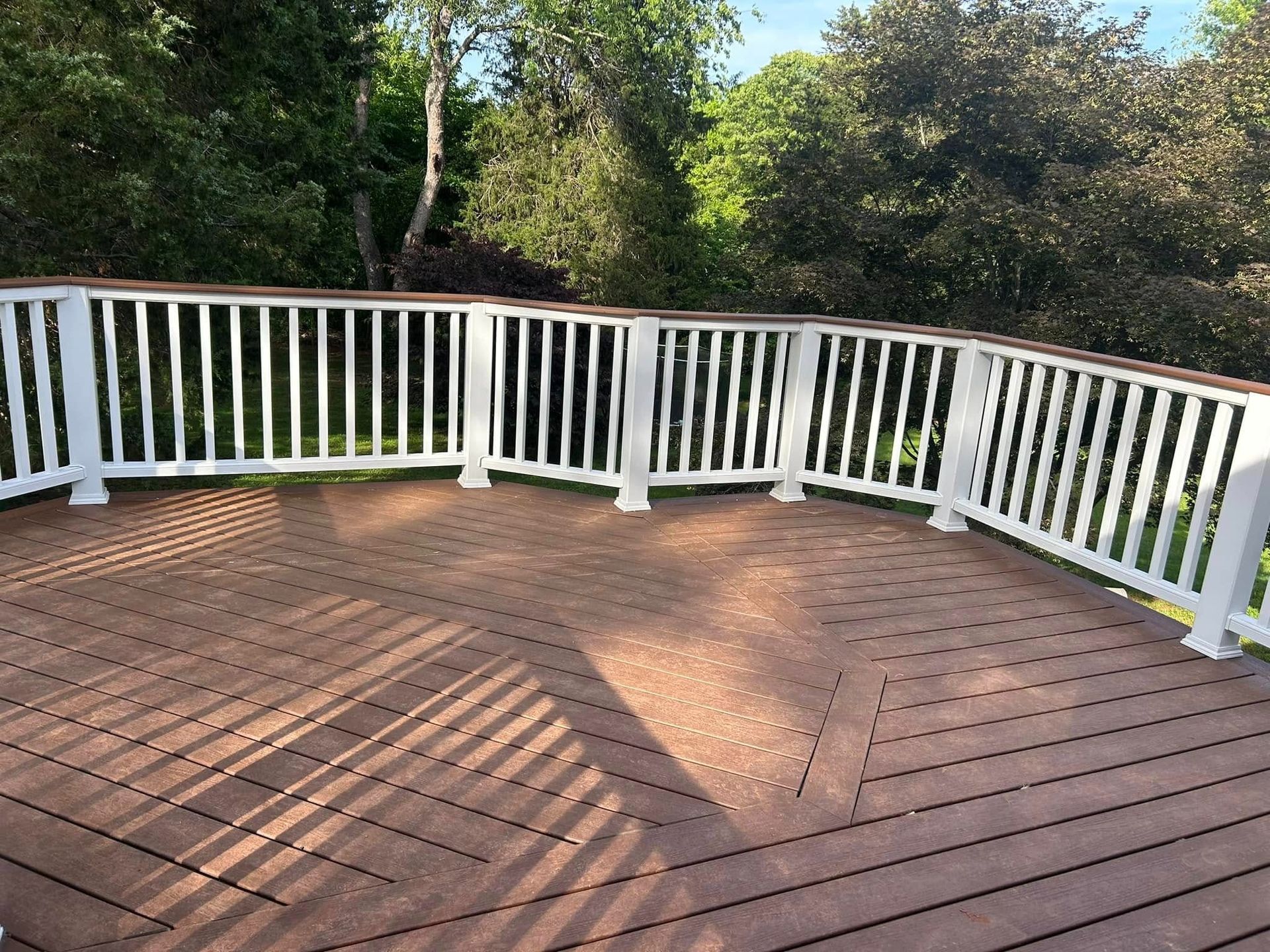 Wooden deck with white railing curving around the edge, overlooking trees in bright sunlight