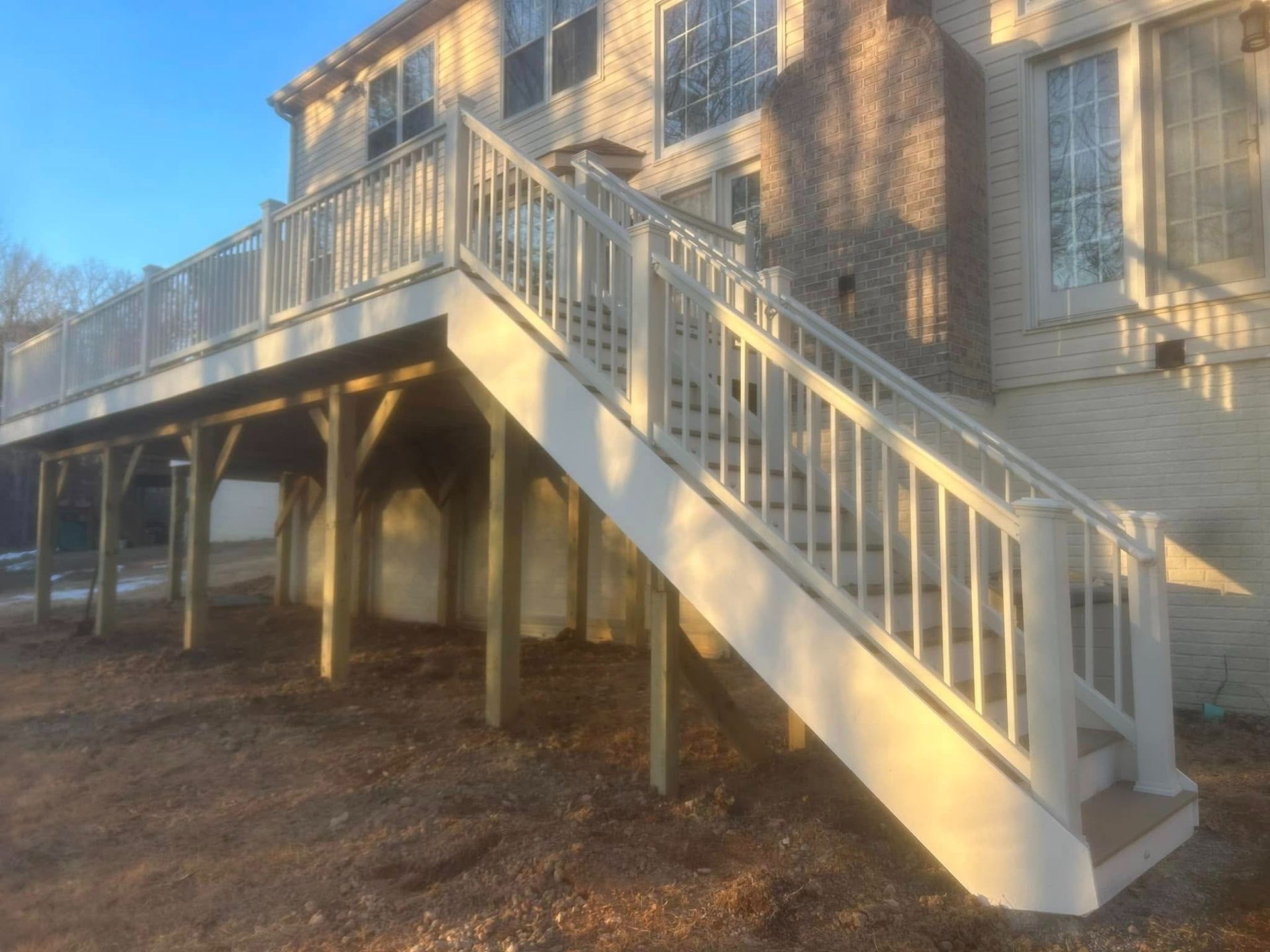White exterior staircase leading to a raised house deck, with railings and sunlit siding