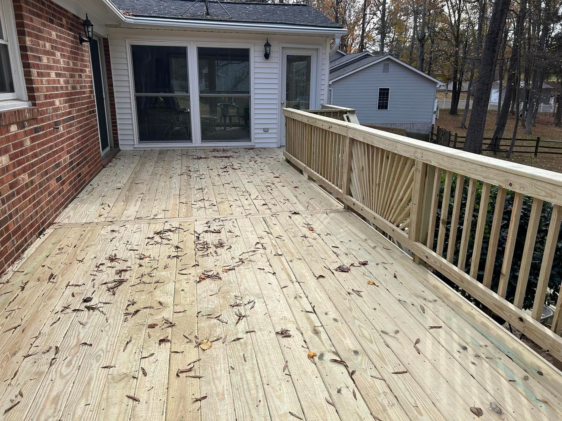 Wooden deck beside a brick house, with railing and sliding glass door overlooking a wooded yard