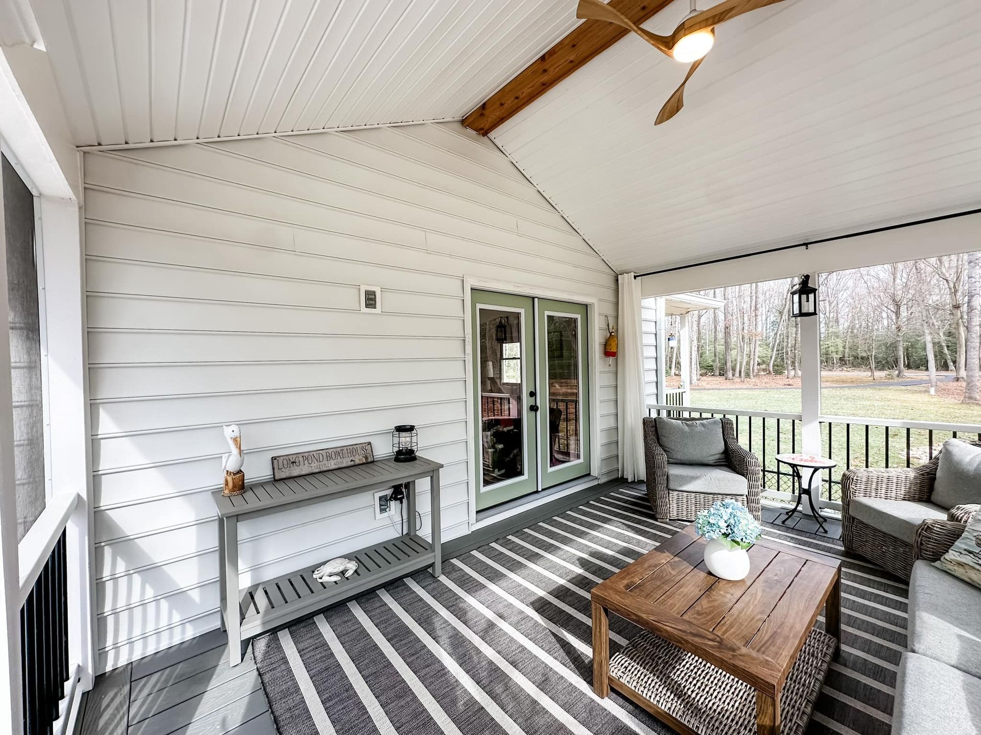 Covered porch with white siding, striped rug, wicker sofa, coffee table, and glass French doors.