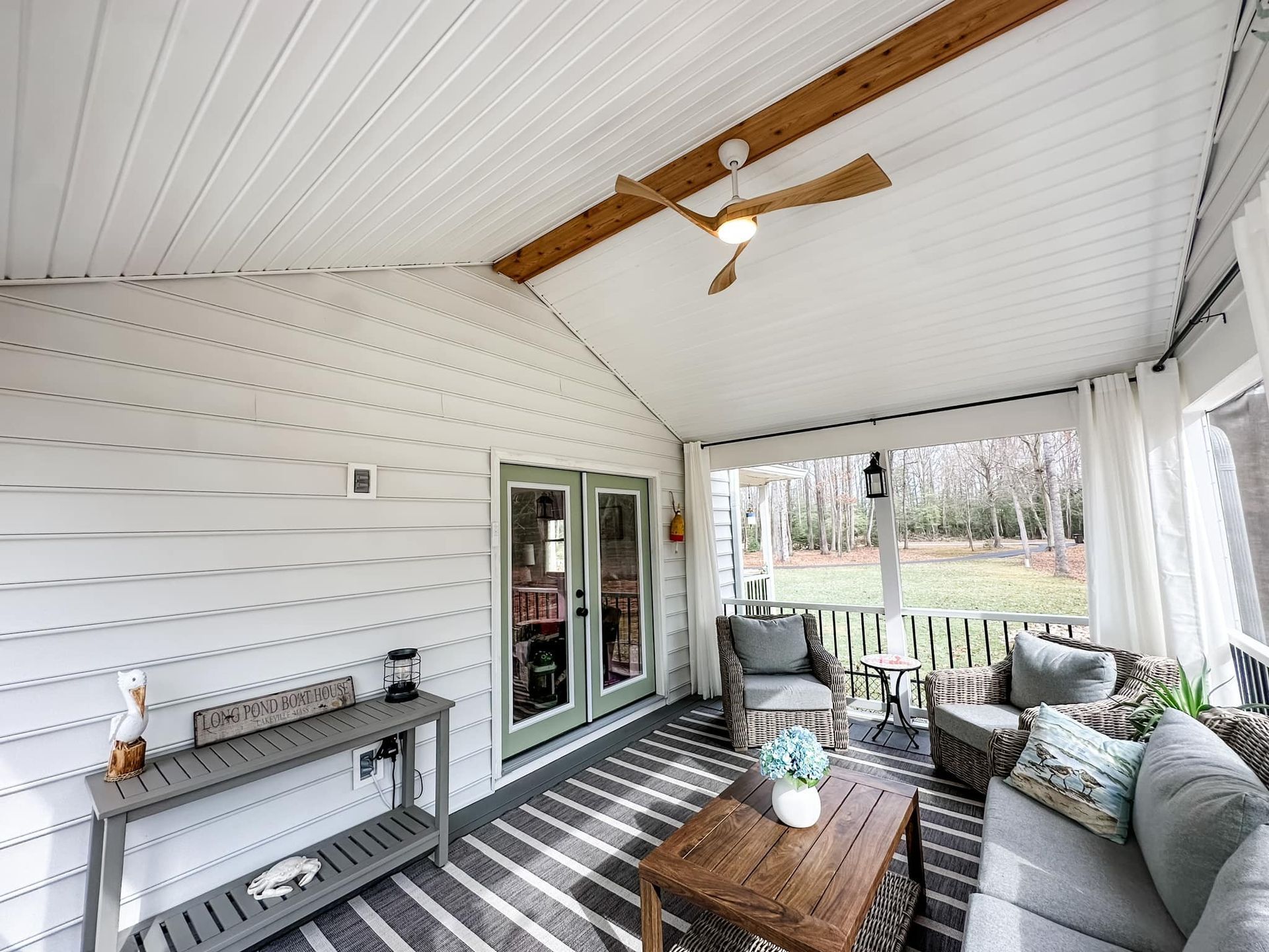 Covered porch with wicker seating, coffee table, ceiling fan, and view of a grassy yard through large openings