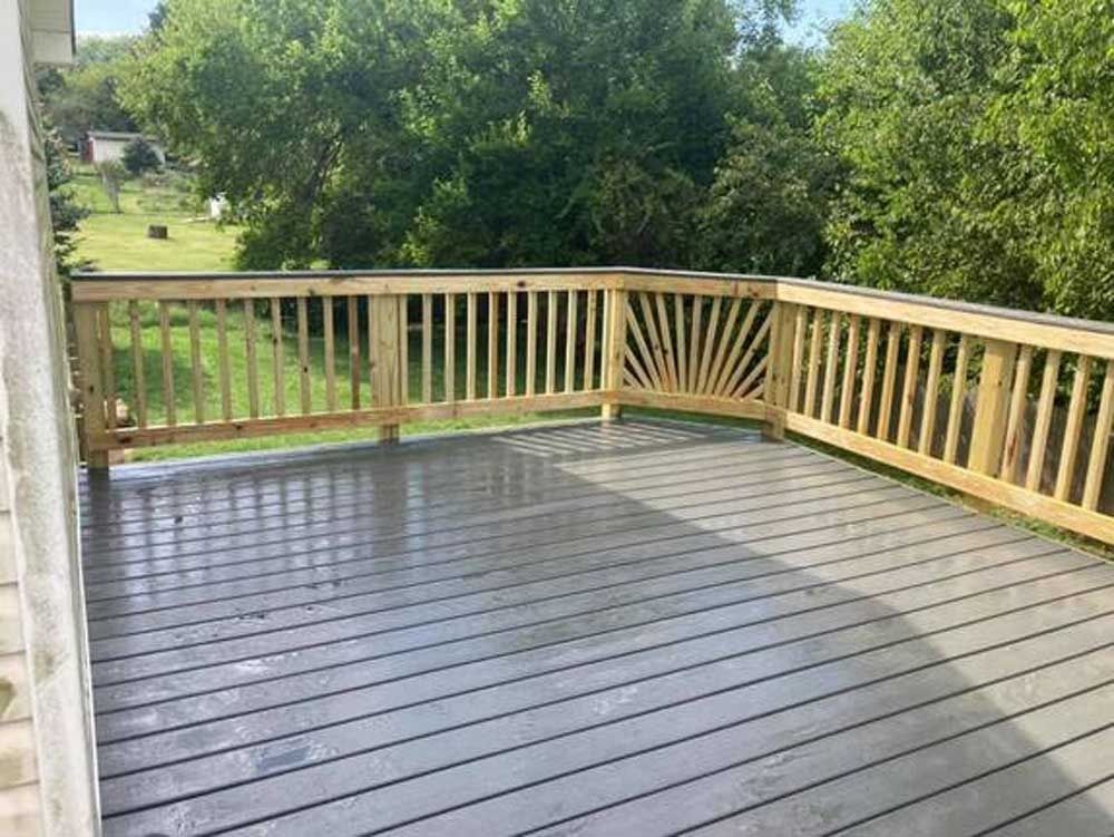 Empty wooden deck with tan railing overlooking a green backyard and trees