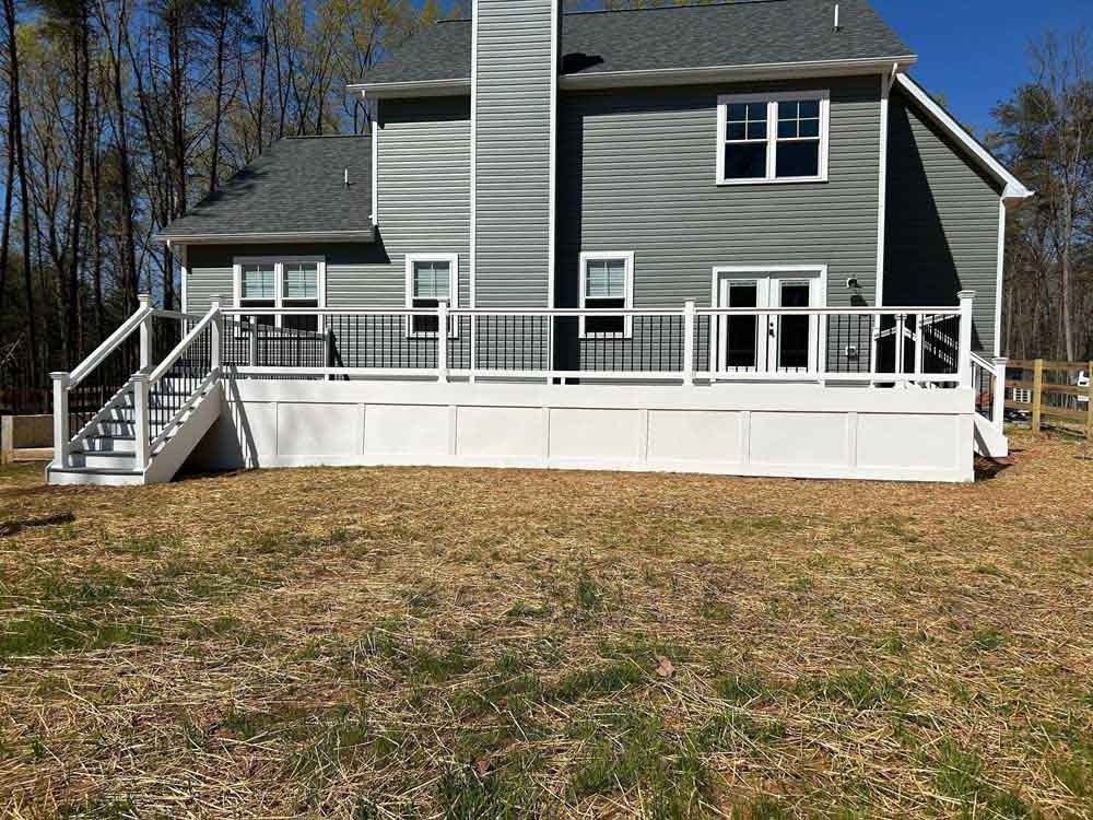 Gray house with white deck and stairs, viewed from a grassy yard in a wooded area