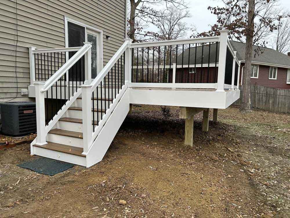 White backyard deck with stairs and railing attached to a beige house