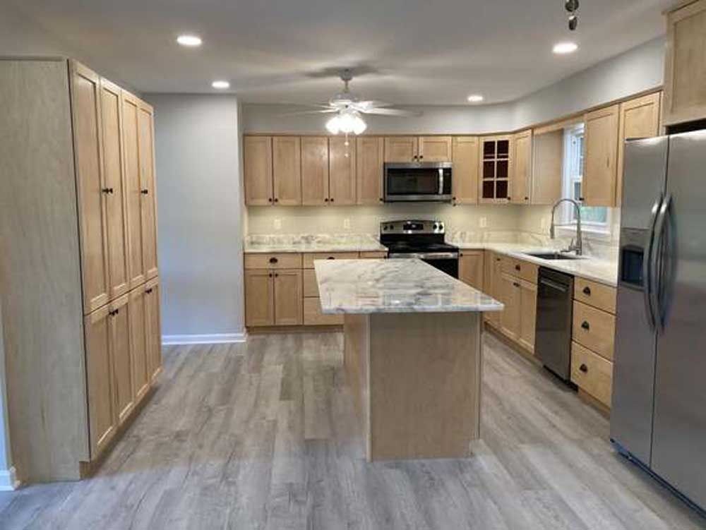 Bright modern kitchen with wood cabinets, marble island, stainless appliances, and gray flooring.