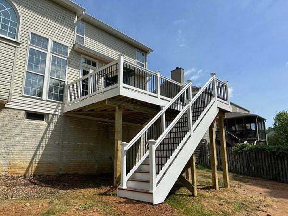 Backyard wooden staircase leading to an elevated deck on a house with white railing and brick siding