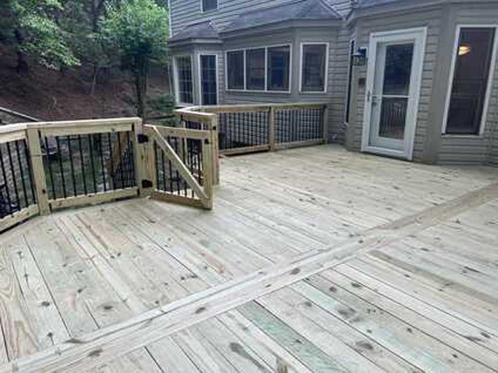 Wooden backyard deck with railing, sliding glass door, and house exterior beside a wooded hillside