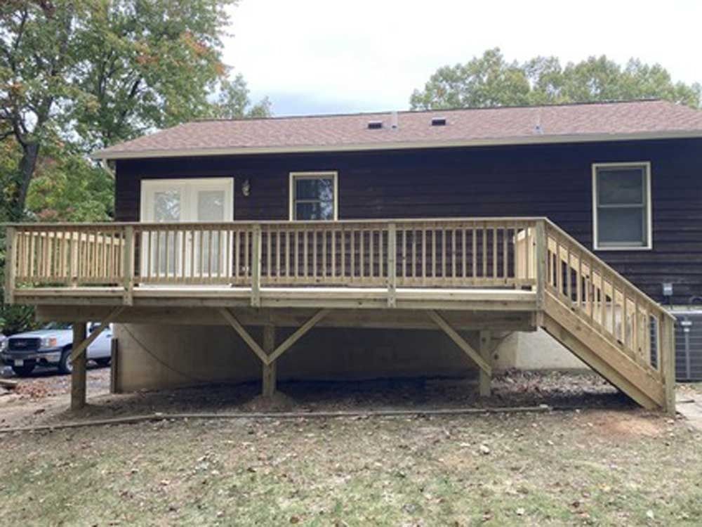Front view of a dark brown house with a raised wooden deck and stairs in a yard.