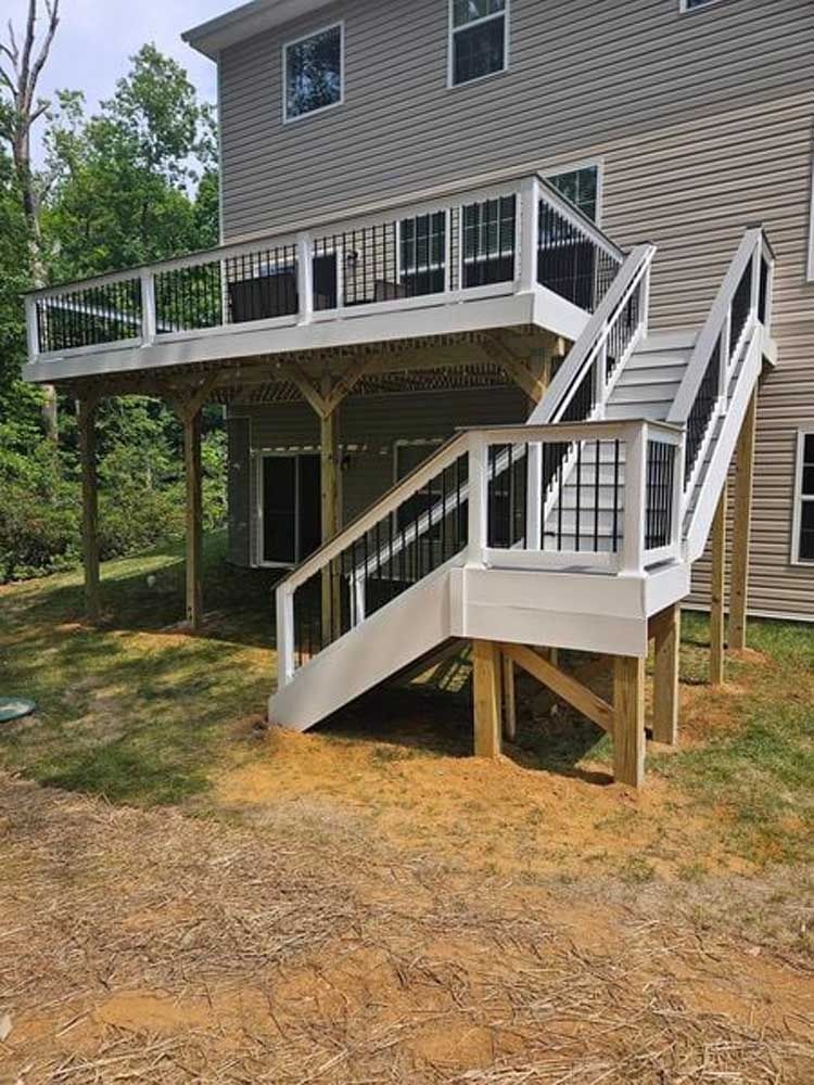 House with elevated deck and white stairs leading to a side entrance in a wooded yard