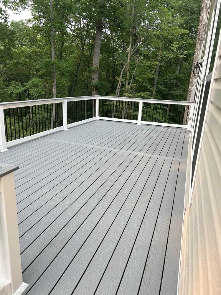 Gray deck with white railings overlooking a wooded backyard