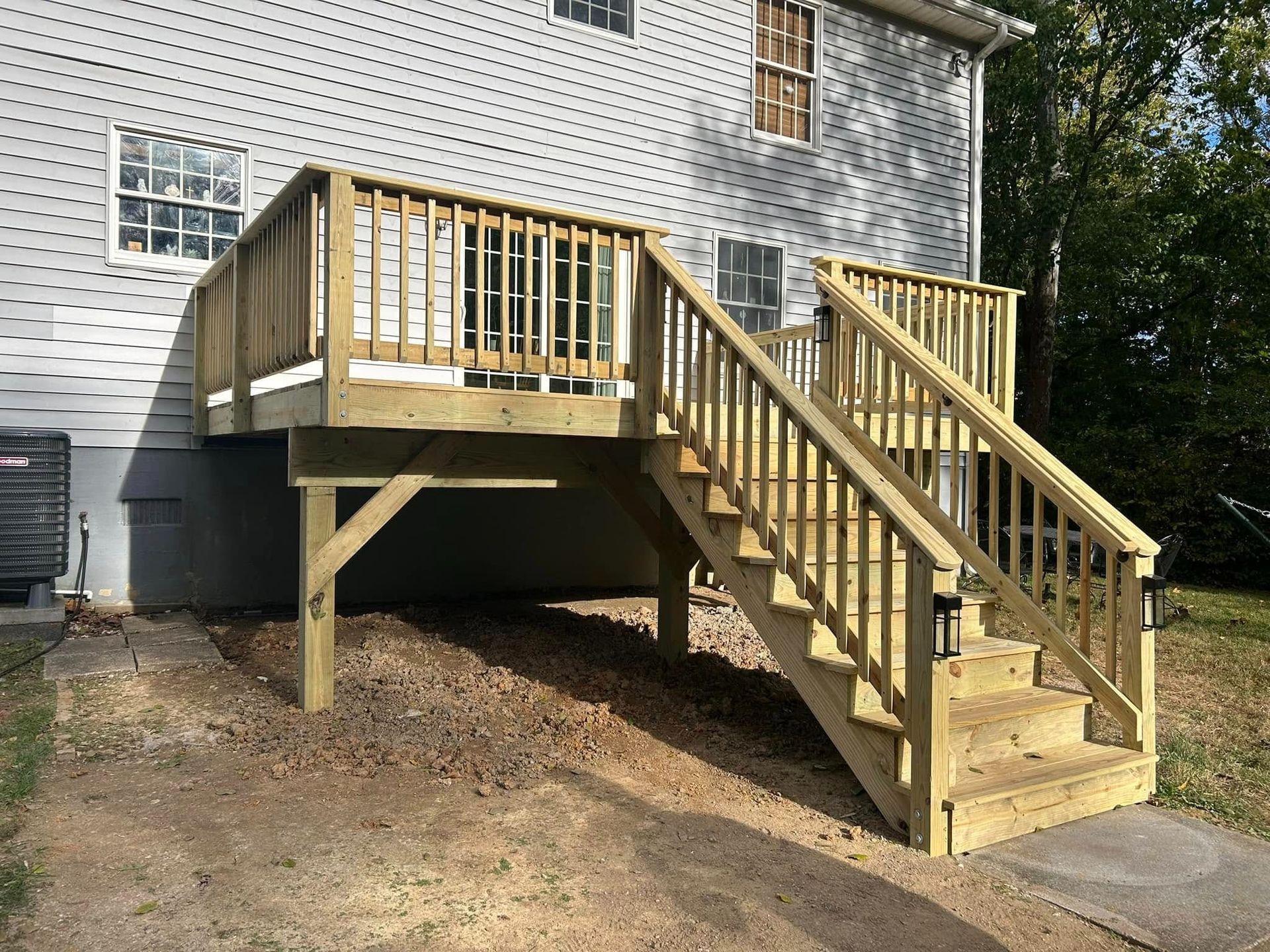 Wooden backyard deck and staircase attached to a house, with a ramp-like sloped support underneath.