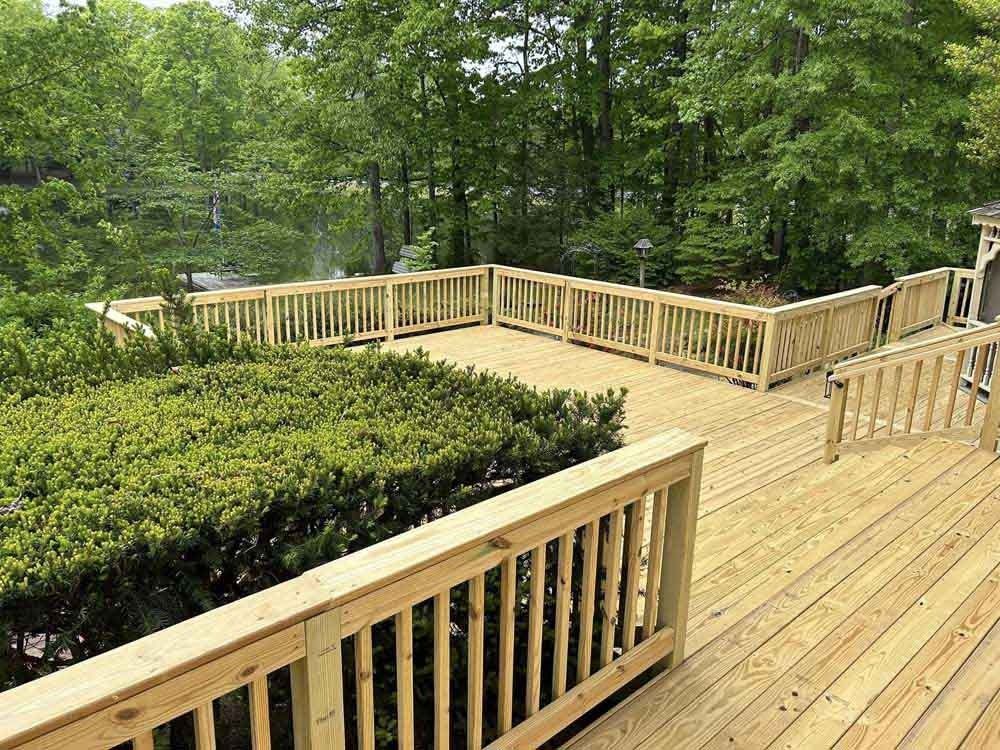 Wooden boardwalk deck with railings beside green shrubs and trees in a wooded park