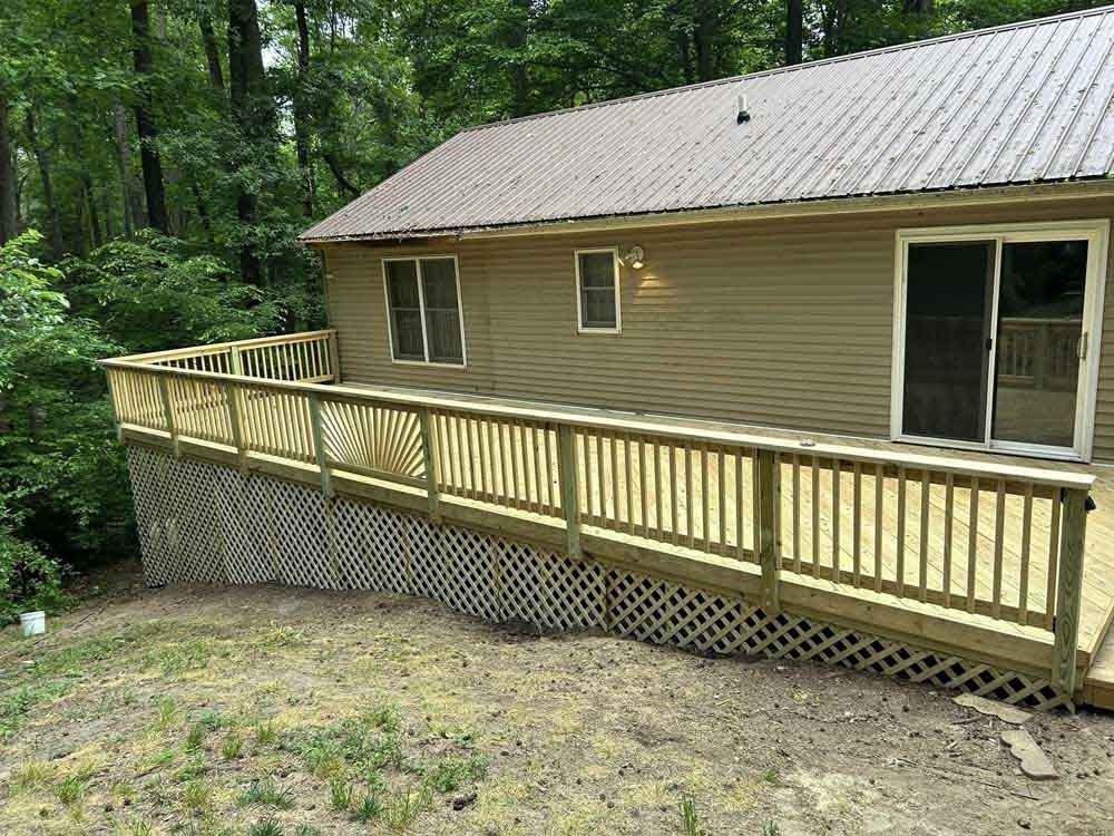Wooden ramp with railing attached to a tan house in a wooded yard