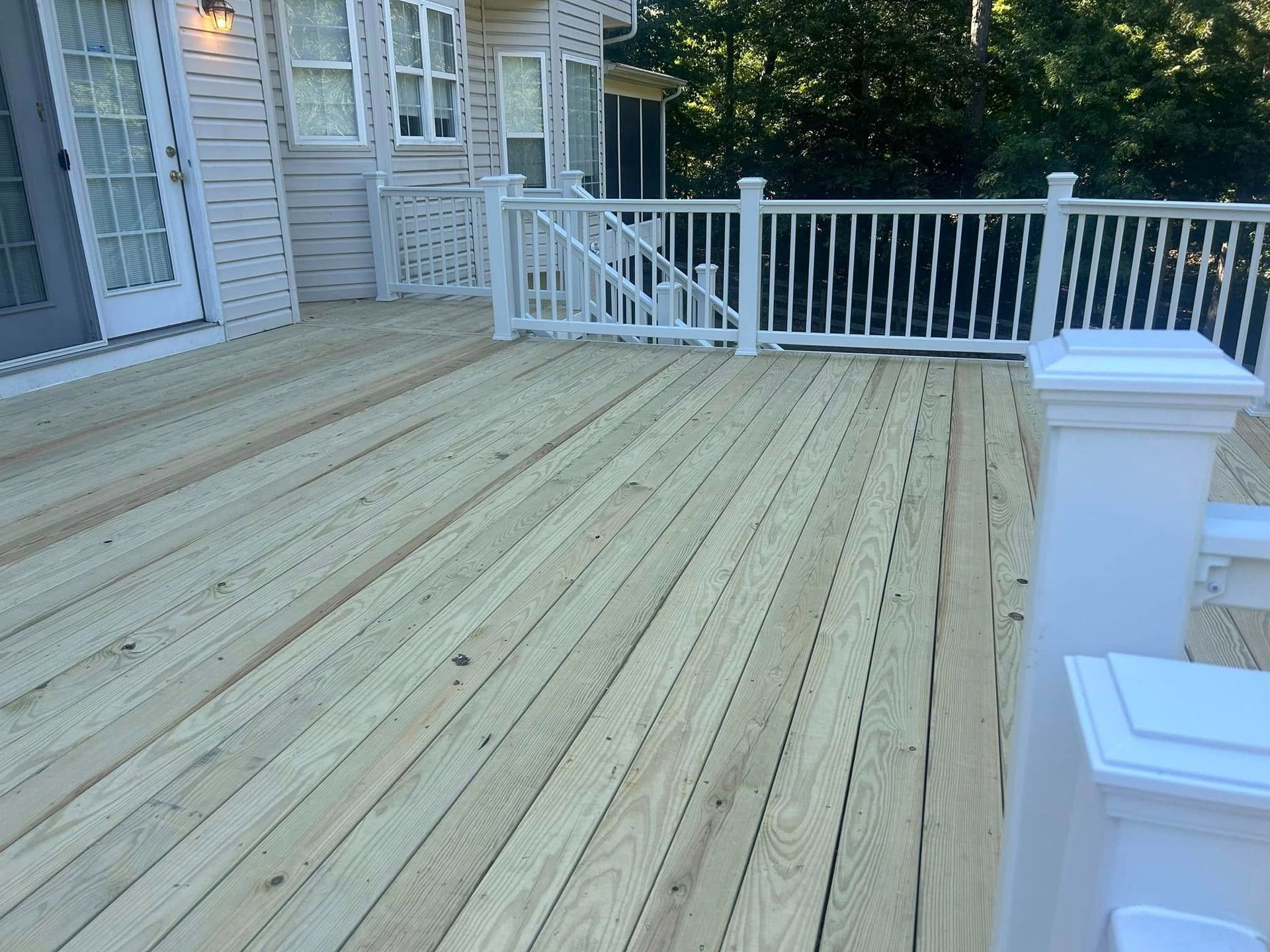 Wooden deck with white railing beside a house, viewed from the corner