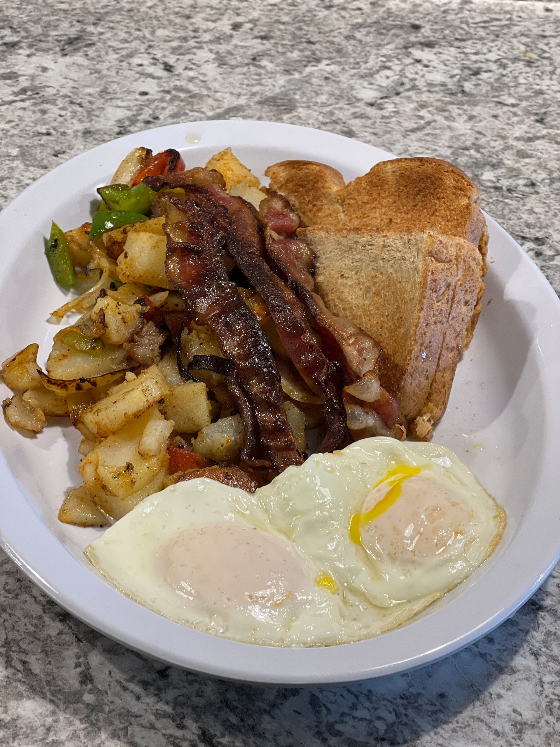 Plate with bacon, potatoes, toast, and two fried eggs on a countertop