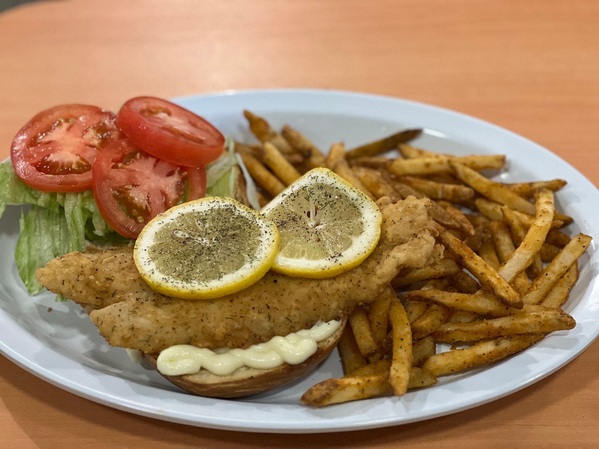 Fried fish, lemon slices, fries, tomato salad, and tartar sauce on a white plate