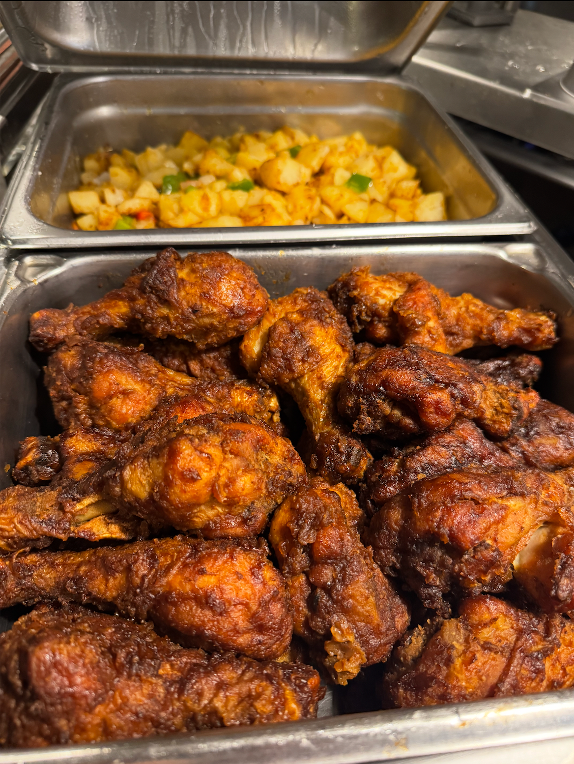 Tray of crispy fried chicken wings with a pan of roasted potatoes in the background