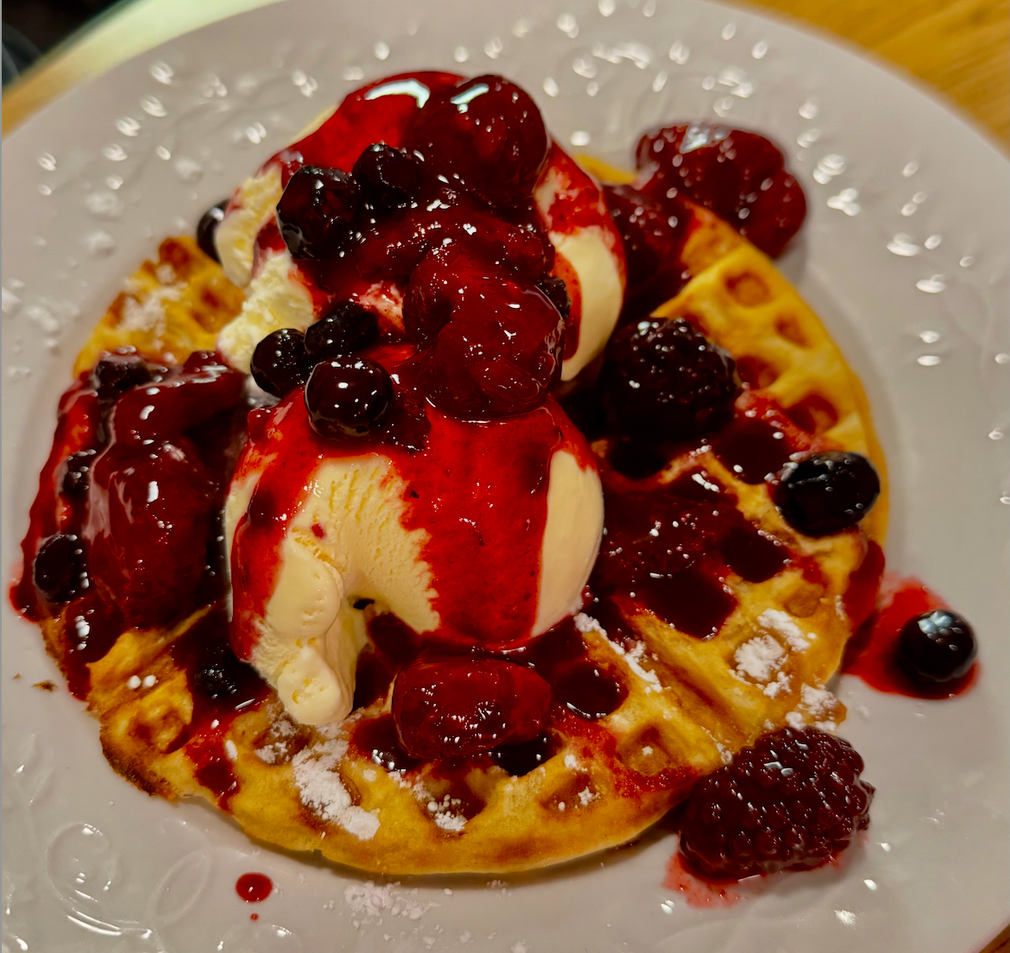 Waffle topped with vanilla ice cream, berry compote, and powdered sugar on a white plate