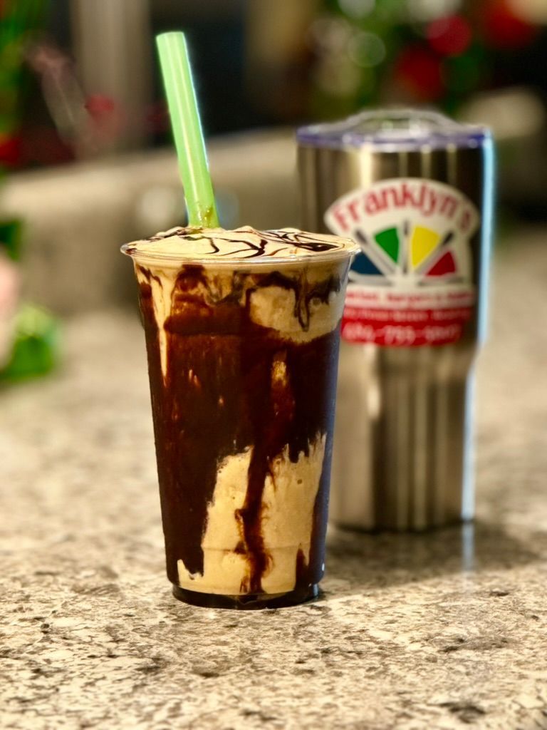 Chocolate milkshake in a clear cup with green straw on a counter, a can blurred in the background