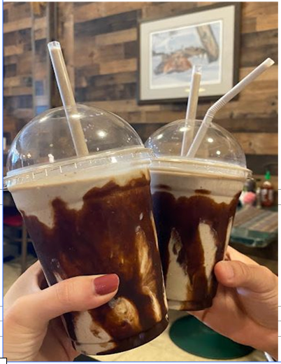 Two hands holding iced coffee drinks with domed lids and straws in a café
