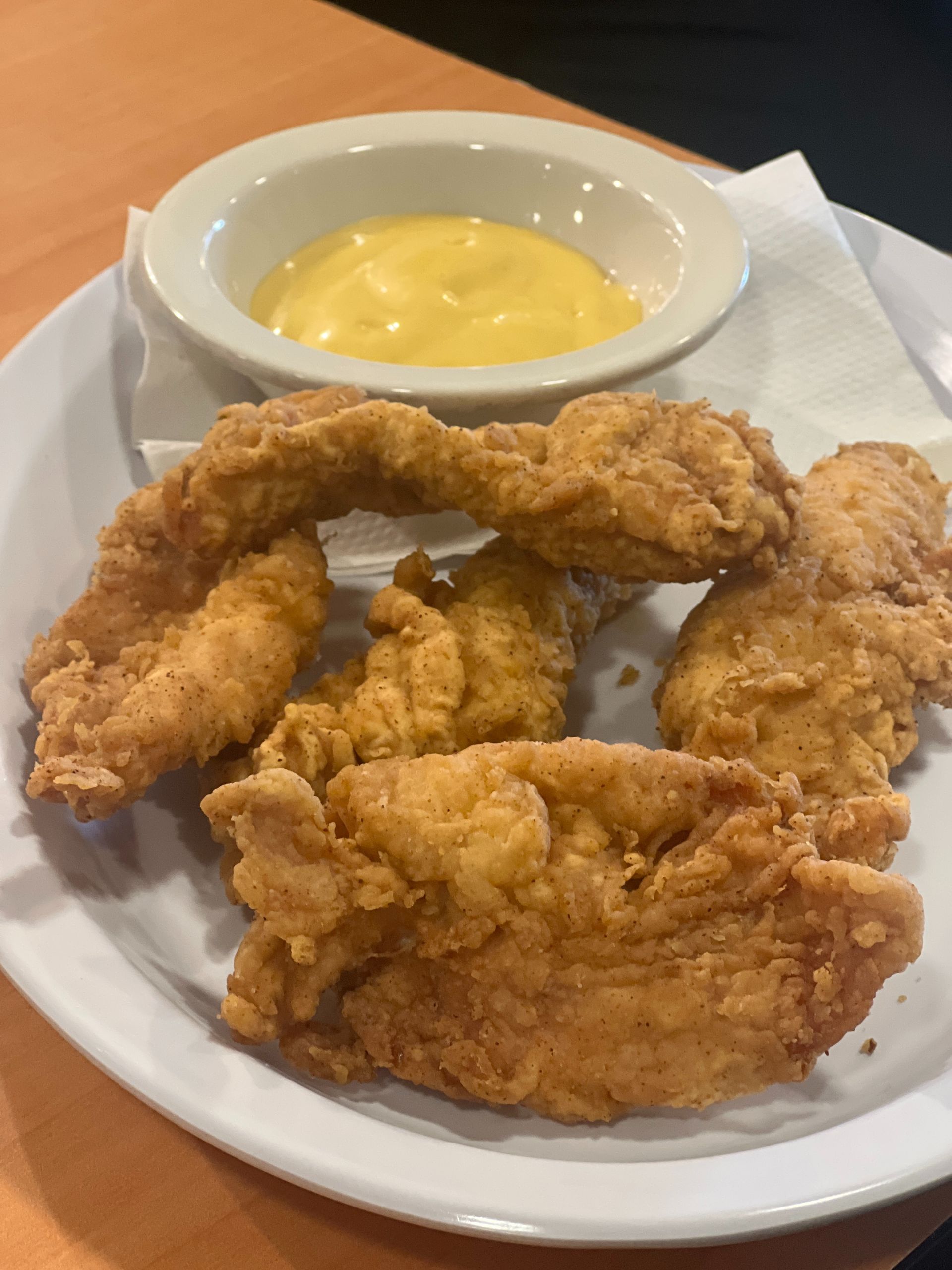Fried chicken tenders on a plate with a side of yellow dipping sauce