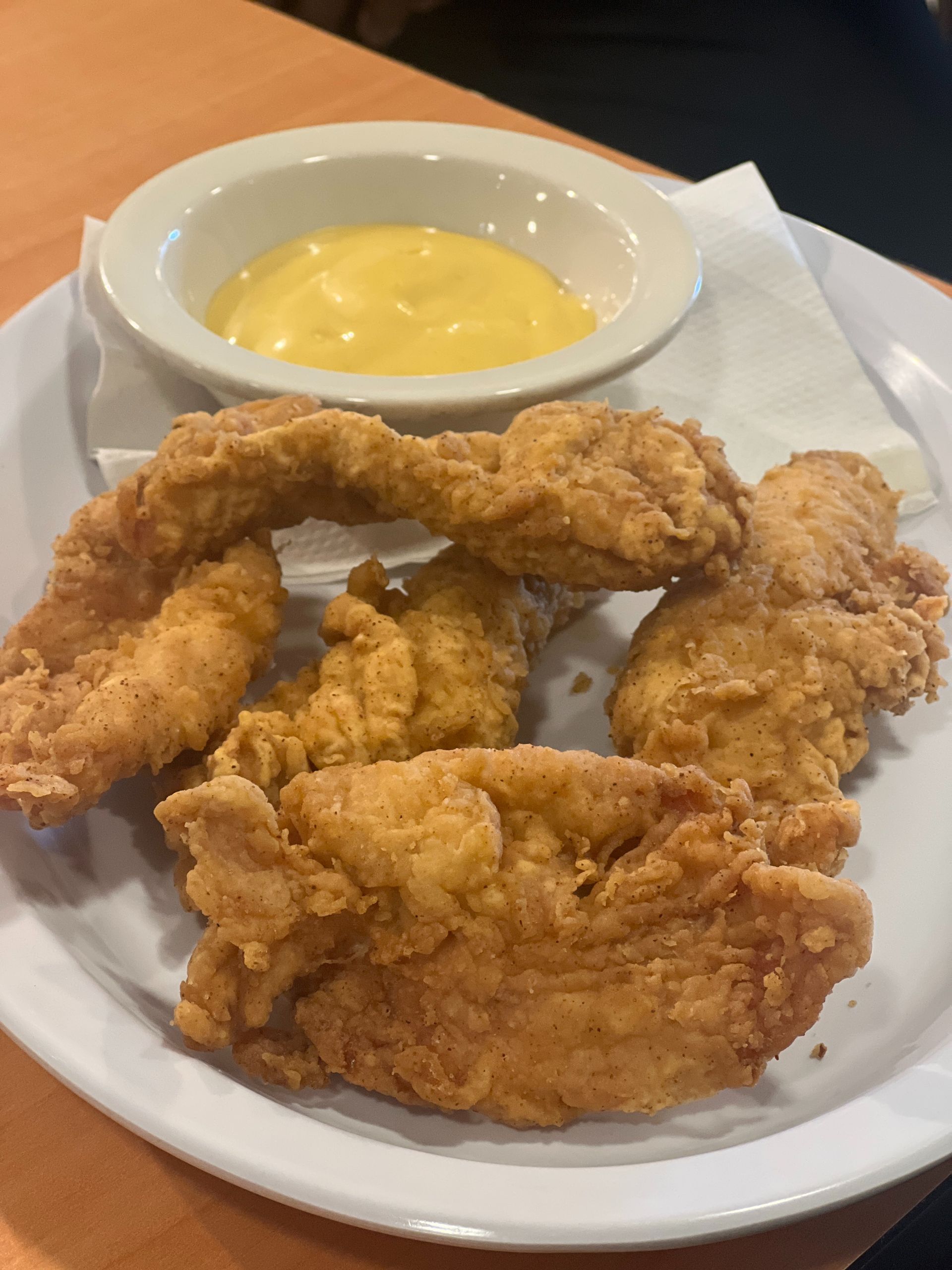 Plate of fried chicken tenders with a side of yellow dipping sauce on a white plate