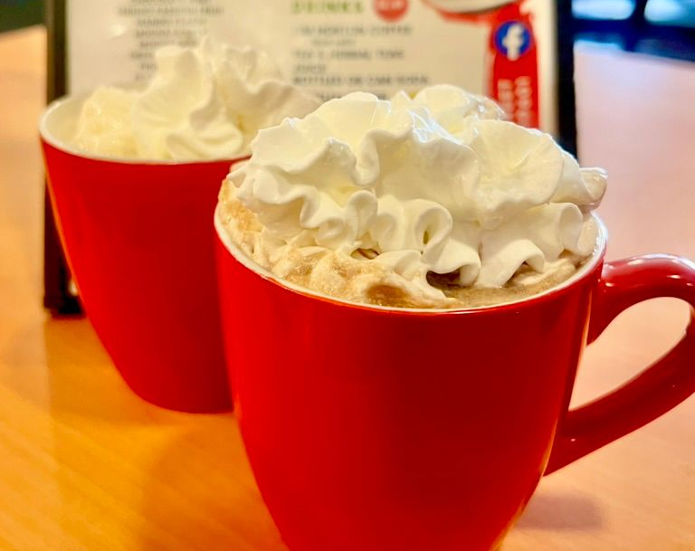 Two red mugs topped with whipped cream on a wooden table
