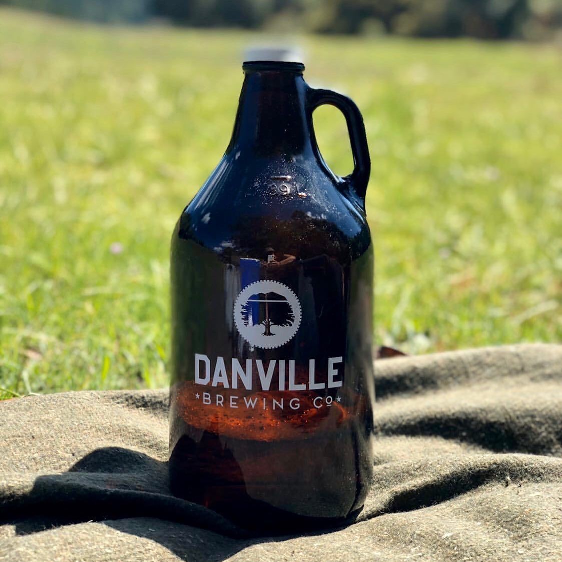 A bottle of danville brewing company beer is sitting on a blanket in the grass.