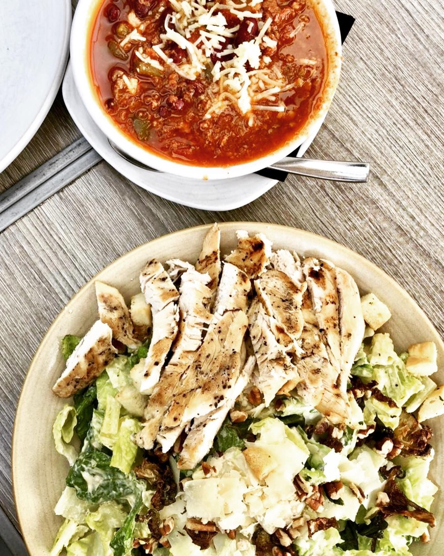 A bowl of chili and a plate of salad are on a table.
