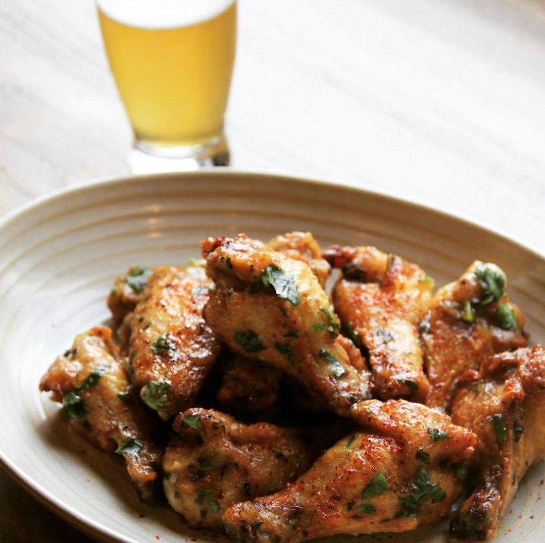 A plate of chicken wings next to a glass of beer