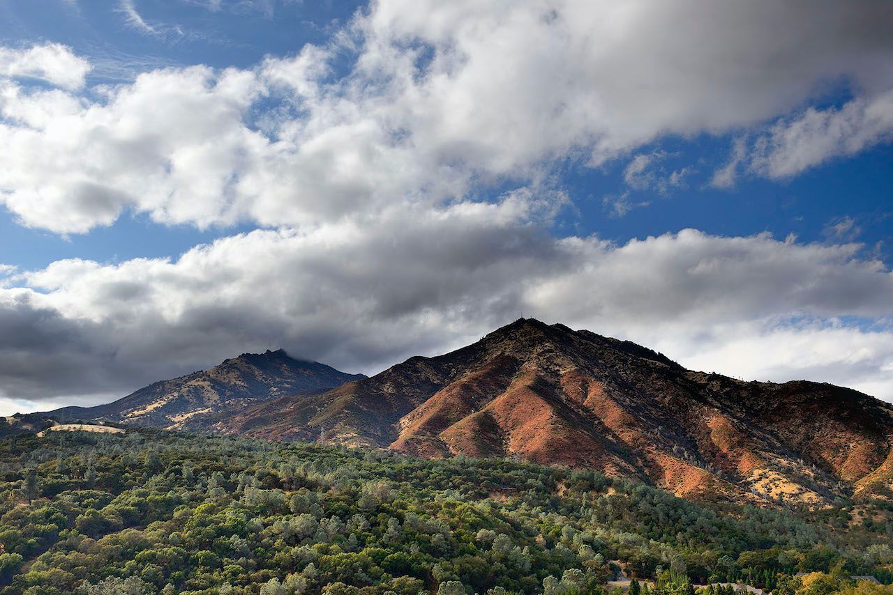 A mountain covered in trees with a cloudy sky in the background.