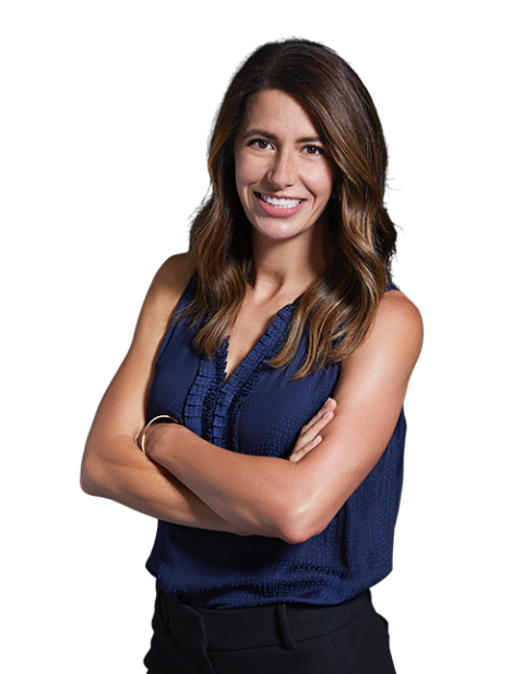 A woman in a blue tank top is standing with her arms crossed and smiling.