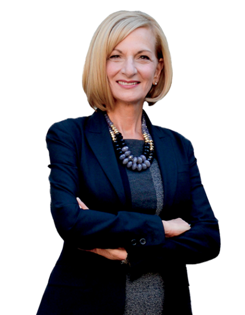 A woman wearing a blue jacket and a necklace is standing with her arms crossed