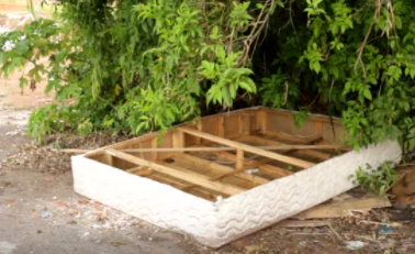 Box spring mattress near road needs to be thrown in garbage.